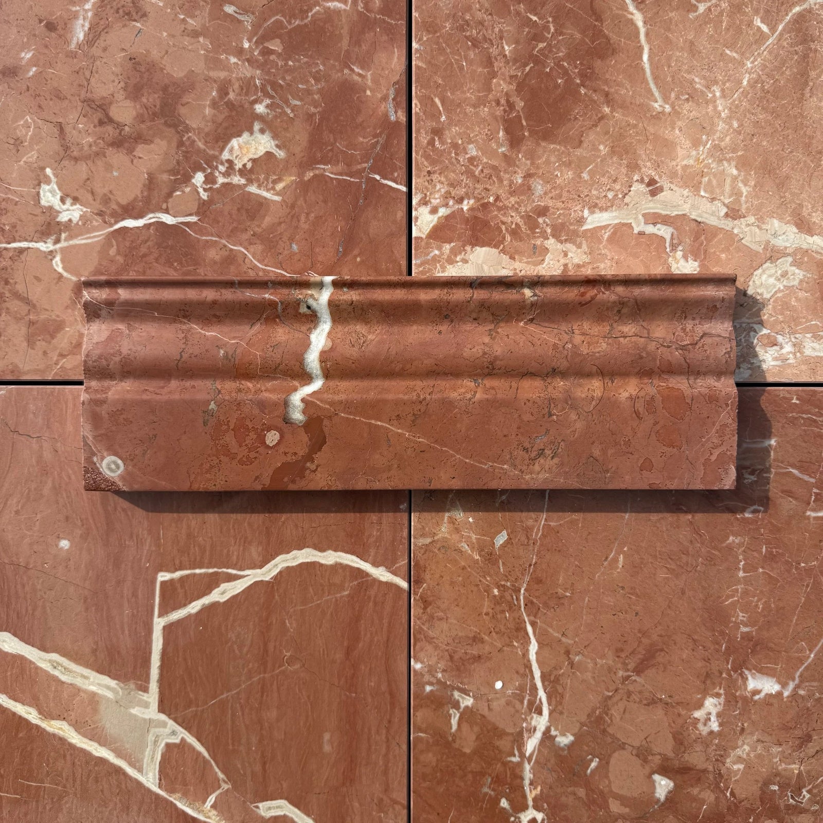 Rojo Alicante marble baseboard by Tilehouz; red marble with white veins on a tile wall background.
