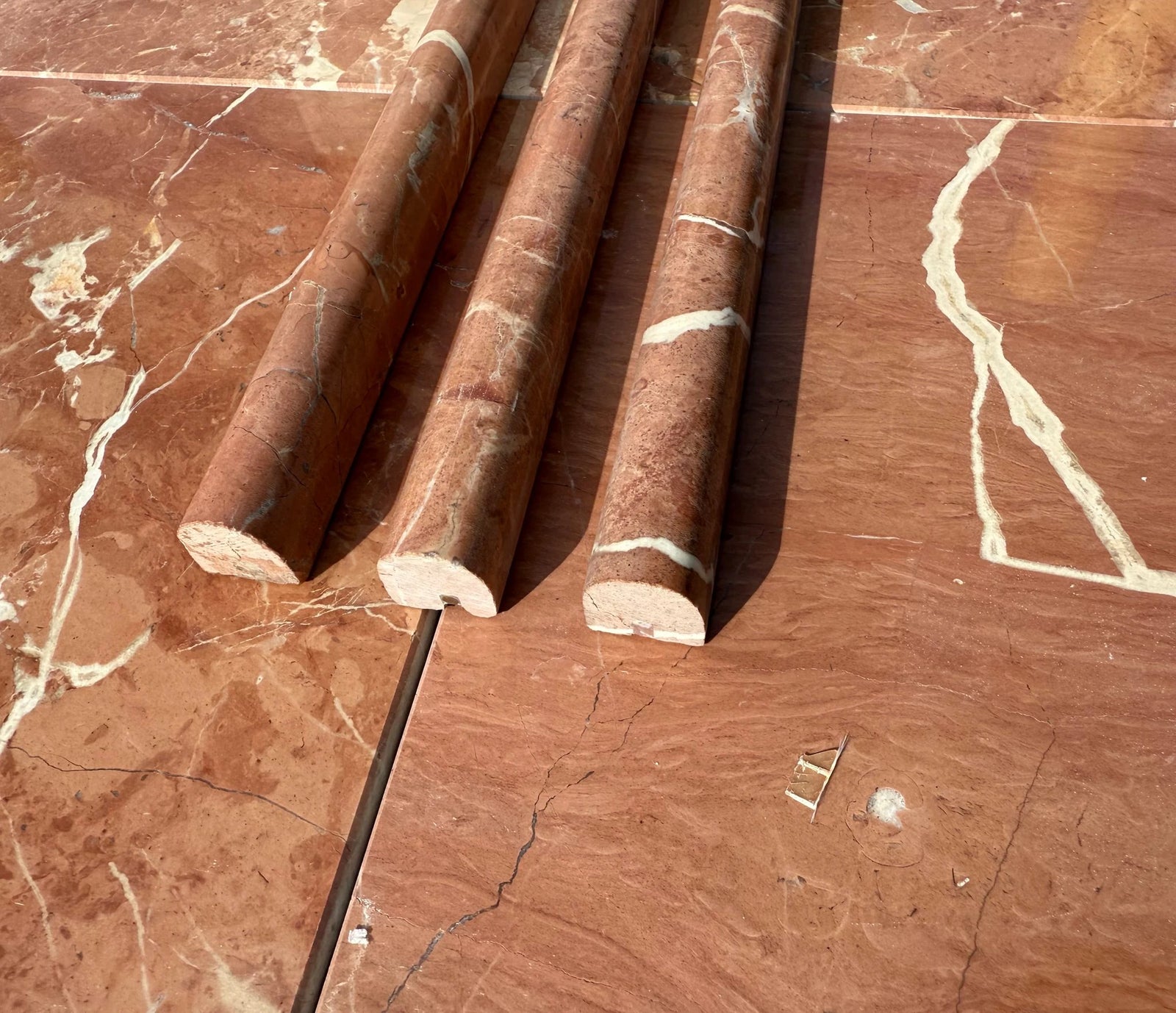 Tilehouz Rojo Alicante marble bullnose liners, 3/4x12, three pieces with red color and white veining.