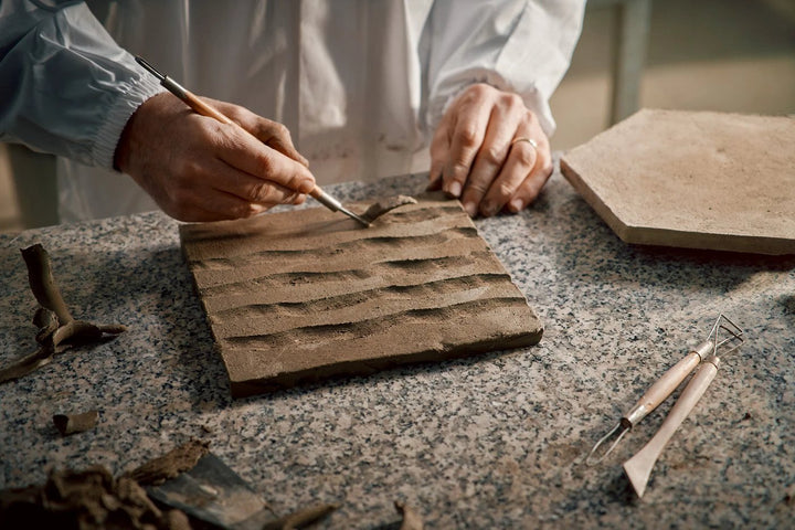 Terracreta intarsio argilla hexagon porcelain tile sample in brown tones being carved on a granite workbench.